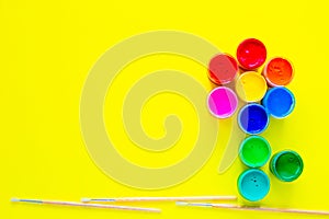 A creative flower made up of cans of paint and brushes for drawing under it on a yellow background with a place for text