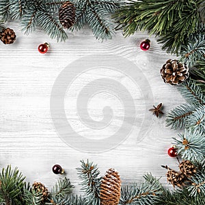 Creative frame made of Christmas fir branches on white wooden background with red decoration