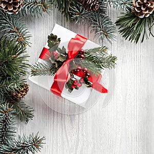 Creative frame made of Christmas fir branches on white wooden background with gift box, pine cones. Xmas and New Year theme.