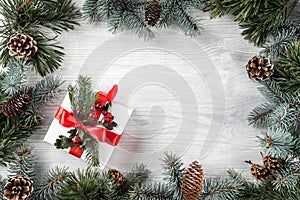 Creative frame made of Christmas fir branches on white wooden background with red decoration