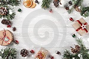 Creative frame made of Christmas fir branches on white wooden background with red decoration, pine cones. Xmas and New Year theme