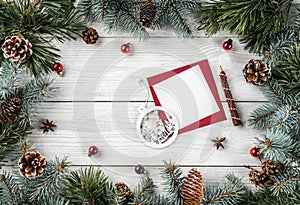 Creative frame made of Christmas tree branches on white wooden background with paper card note, pine cones, balls