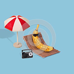 Creative fun idea with a banana in sunglasses lying on a sun bed and listening to music on the radio on the beach