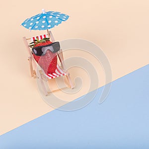 Creative fun idea made of deck chair, sun umbrella and strawberry with sunglasses on a beach