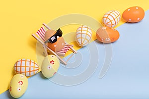 Creative funny composition with Easter egg with sunglasses while sitting on deck chair and colored eggs on illuminating yellow and