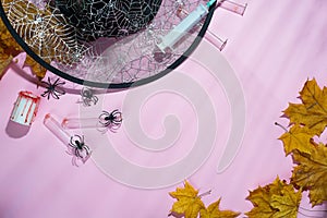 Creative halloween concept photo of witches hat, spiders and syringes with deep shadows on soft pink background