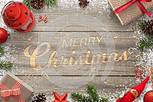 Creative hand carved Merry Christmas text in a wooden surface. Surrounded with Christmas decorations