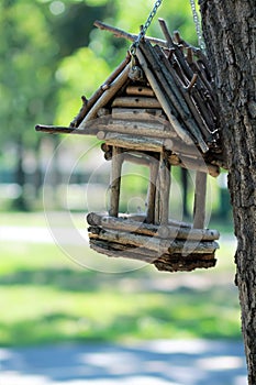 Creative hand made wooden bird house/bird feeder hanging on a chain on the tree in a park