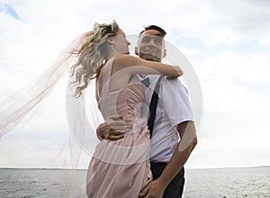 Creative hipster wedding by the sea. The bride is in a pink dress and veil, the groom is in beautiful trousers with suspenders and