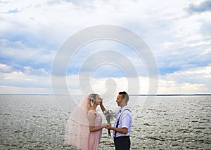 Creative hipster wedding by the sea. The bride is in a pink dress and veil, the groom is in beautiful trousers with suspenders and