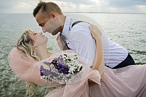 Creative hipster wedding by the sea. The bride is in a pink dress and veil, the groom is in beautiful trousers with suspenders and