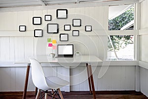 Creative home office interior with laptop blank screen, picture frame, chair, cup coffee, flower pot on desk