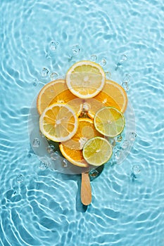 Creative ice lolly made from citrus fruit slices in blue water background with concentric circles and ripples