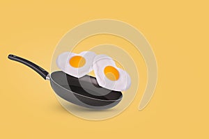 Creative idea with a frying pan and a flying fried egg in heart shape on a yellow background. Minimal food and love concept