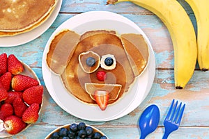 Creative idea for kids breakfast. Dog shaped pancakes with berries on blue wooden table, top view. Healthy food for