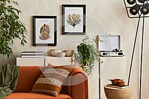Creative interior composition of living room with designed couch, two mock up poster frames, coffee table, plants, industrial lamp