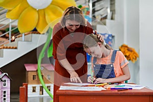 Creative kids during an art class in a daycare center or elementary school classroom drawing with female teacher.