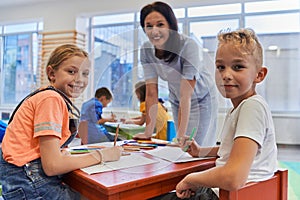 Creative kids during an art class in a daycare center or elementary school classroom drawing with female teacher.