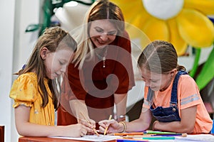 Creative kids during an art class in a daycare center or elementary school classroom drawing with female teacher.