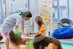 Creative kids during an art class in a daycare center or elementary school classroom drawing with female teacher.