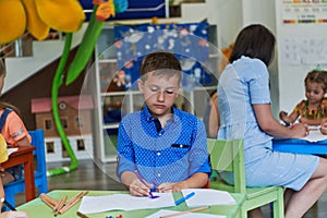 Creative kids during an art class in a daycare center or elementary school classroom drawing with female teacher.