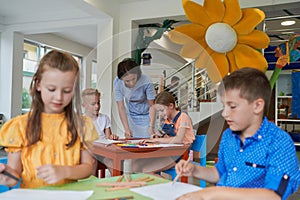 Creative kids during an art class in a daycare center or elementary school classroom drawing with female teacher.