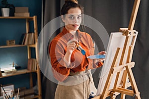 Creative latin female artist standing working on a new painting. Happy young lady painting on canvas in her art studio