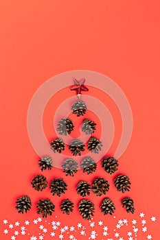 Creative layout of Christmas tree made of fir cones, star, with white snowflakes and sequins as snow on red background. Flat lay,