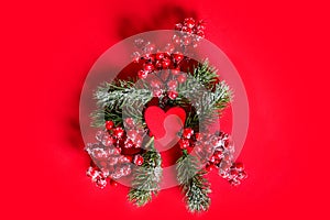 Creative layout made of Christmas tree branches with red berries and red wooden heart in the middle