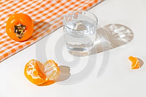 Creative layout made of fresh orange tangerin, persimmon fruit and a glass of water on cage kitchen towel and white background.