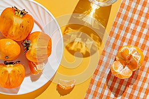 Creative layout made of fresh persimmon fruits and orange tangerin on bright background with shadow. Healthy food concept. Summer