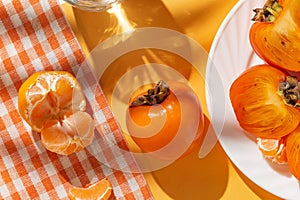 Creative layout made of fresh persimmon fruits and orange tangerin on bright background with shadow. Healthy food concept. Summer