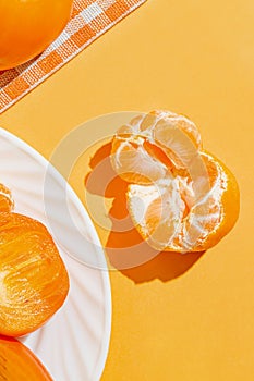 Creative layout made of orange mandarin closeup, fresh persimmon fruits on white plate on bright background with shadow. Healthy