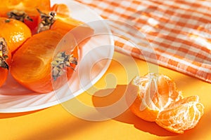Creative layout made of orange mandarin, fresh persimmon fruits on white plate on bright background with shadow. Healthy food