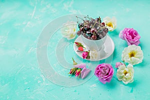 Creative layout made with blossoming flowers and cup with berries on blue background. Flat lay layout with cherries and