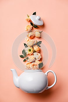 Creative layout made of whte tea pot with orange roses on pink background