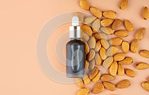 Creative layout. Natural almond oil in a matte glass bottle and scattering of almonds on a pastel beige background. The