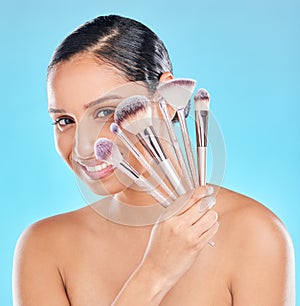 Creative, makeup and portrait of girl with brushes in hand to apply cosmetics in blue background. Studio, beauty and