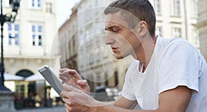 Creative man sitting on sidewalk and using tablet computer