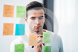 Creative man writing sticky note on glass wall at office space