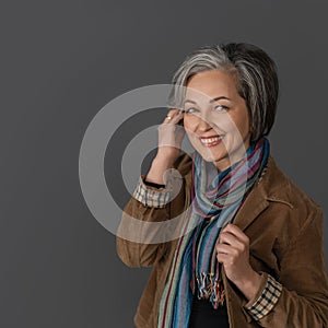 Creative mature woman in casual touching her graying short hair. Studio portrait on gray background. Copy space at left