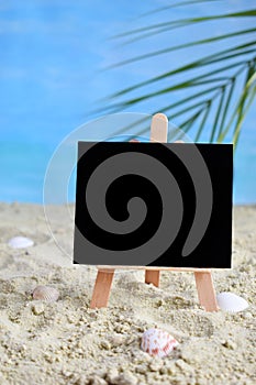 Creative minimal summer idea. Blackboard on sand with blur blue sea and tropical palm leaf. Vacation promotion sale concept. Creat