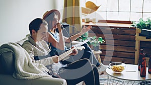 Creative musical duet is practising at home woman is singing in microphone and man is playing the guitar. Young cheerful