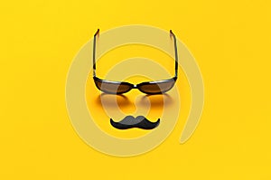 Creative party decoration concept. Black mustache, sunglasses, props for photo booths, carnival parties on yellow background top