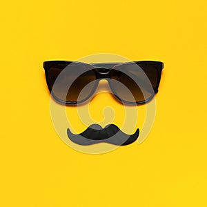 Creative party decoration concept. Black mustache, sunglasses, props for photo booths, carnival parties on yellow background top