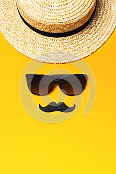 Creative party decoration concept. Black mustache, sunglasses, straw hat, carnival parties on yellow background top view flat lay