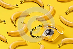 Creative pattern bananas and old yellow phone with hard shadows pattern on yellow background flat lay