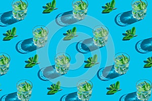 Creative pattern made of and glass with lemonade or water with mint leaves on blue background. Summer refreshment concept. Minimal