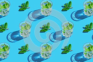 Creative pattern made of and glass with lemonade or water with mint leaves on blue background. Summer refreshment concept. Minimal