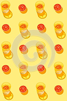 Creative pattern made with sliced blood orange and glass with lemonade or water on yellow background. Summer fruit and refreshment